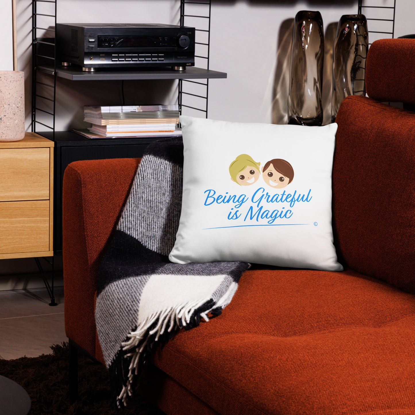 Whimsical 18x18 throw pillow spreading positivity with the enchanting words 'Being Grateful is Magic,' enhancing a red couch and a stylish checkered scarf.