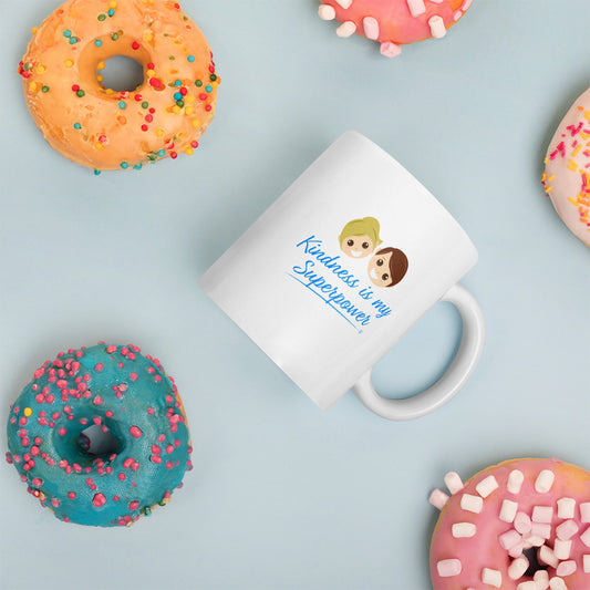 A white mug featuring the uplifting quote 'Kindness is my Superpower' surrounded by delicious donuts in the background.